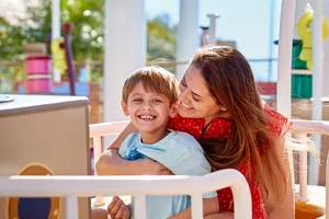 A mother and son enjoy riding Grandad Dog's Pirate Boat Ride at Peppa Pig Theme Park in Dallas Fort Worth. They smile and laugh as they sail along in the colorful pirate-themed boat, surrounded by the playful and exciting atmosphere of the park.