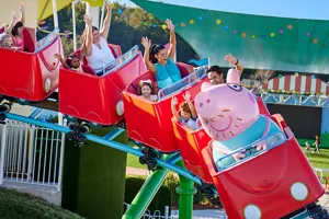 Visitors enjoy the thrill of Daddy Pig's Rollercoaster ride at Peppa Pig Theme Park in Dallas Fort Worth, smiling and laughing as they experience the exciting ride together.