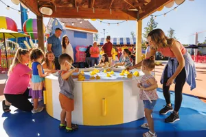Families enjoy playing at the Fun Fair attraction at Peppa Pig Theme Park in Dallas Fort Worth. Children try their luck at picking up ducks at the Lucky Duck Pond, surrounded by the colorful, festive atmosphere of the park.