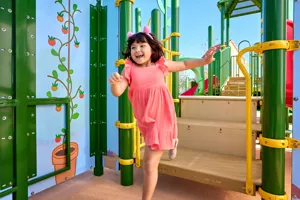 A girl plays at Peppa's Treehouse attraction at Peppa Pig Theme Park in Dallas Fort Worth. She climbs and explores the colorful, interactive treehouse, smiling as she enjoys the fun and imaginative play in the lively park setting.
