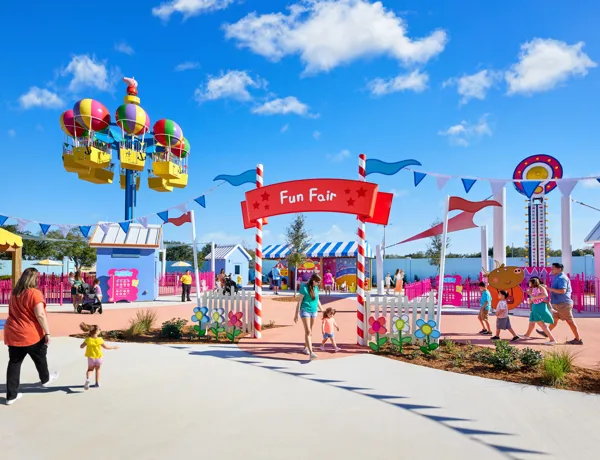 Visitors enjoy the Fun Fair attraction at Peppa Pig Theme Park in Dallas Fort Worth, playing various games and riding the exciting attractions. Laughter fills the air as families experience the playful, colorful atmosphere of the park, creating fun memories together.