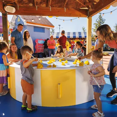Families enjoy playing at the Fun Fair attraction at Peppa Pig Theme Park in Dallas Fort Worth. Children try their luck at picking up ducks at the Lucky Duck Pond, surrounded by the colorful, festive atmosphere of the park.