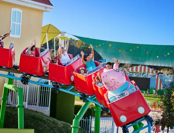 Visitors enjoy the thrill of Daddy Pig's Rollercoaster ride at Peppa Pig Theme Park in Dallas Fort Worth, smiling and laughing as they experience the exciting ride together.